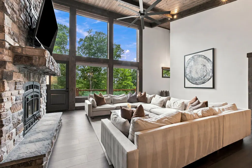 The great room: two-story windows onto the trees, a woodstove set in the stone wall, and the sectional the room was designed around.