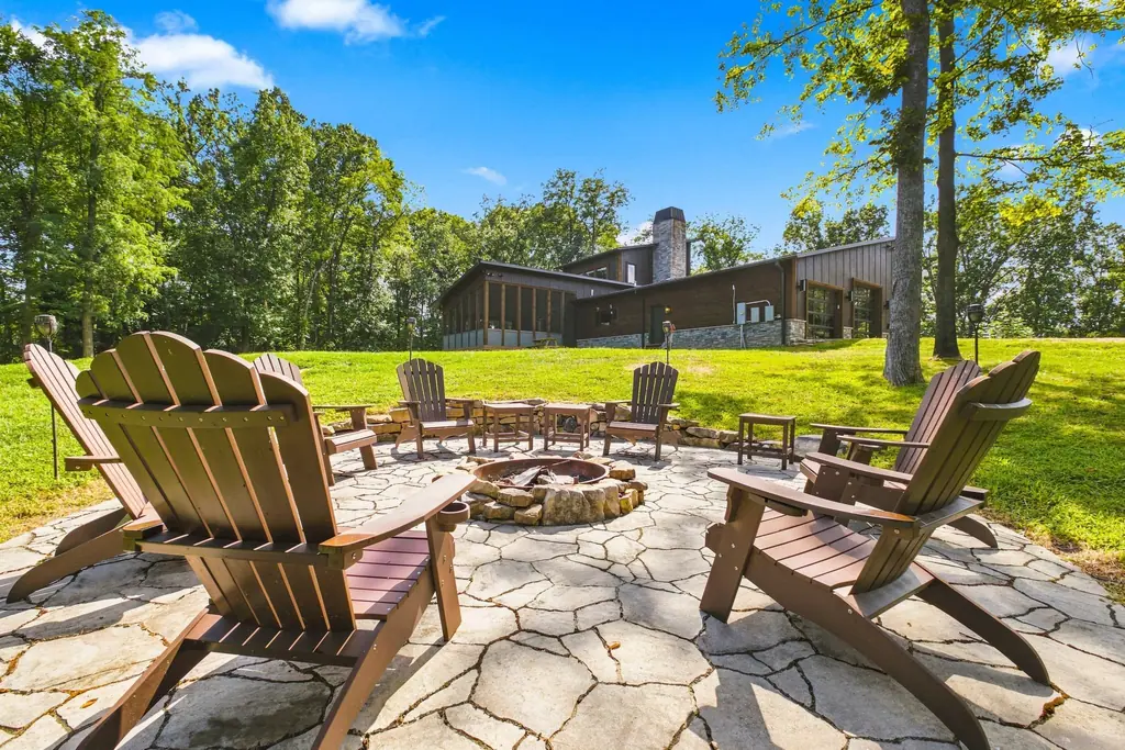 A flagstone firepit ringed with Adirondack chairs, with the house and screened porch on the hill behind.